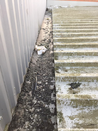 Dirt and debris accumulated along the base of a metal fence beside concrete steps
